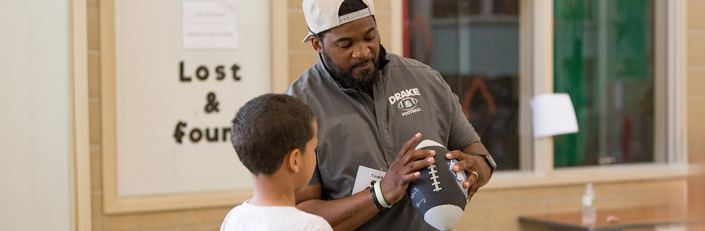 Drake football coach showing student how to hold football